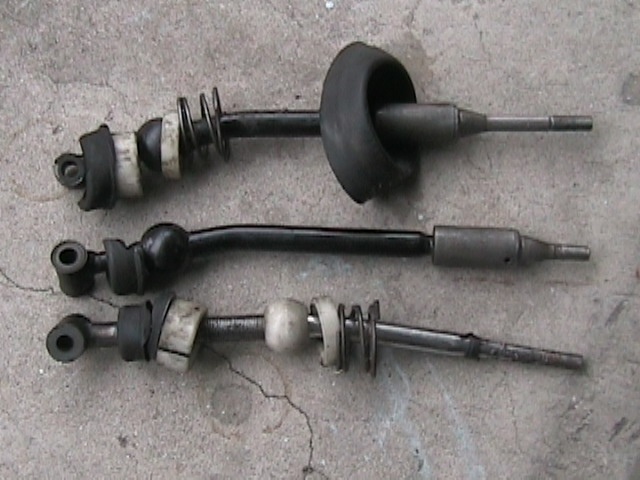 Three car shifter shafts with rubber boots and springs laid out on a concrete surface
