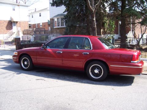 1999 Ford Crown Victoria - Side view of a red sedan parked on a residential street. The body style suggests a 1998 model year.