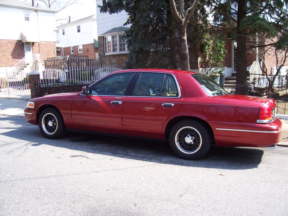 Red sedan parked on street, side view. Appears to be a 1998 model