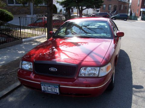 1999 Ford Crown Victoria - A red Ford Crown Victoria is parked on a street, showing its front grille and headlights.