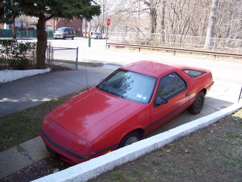 1999 Ford Crown Victoria - A red coupe is parked on a sidewalk, with its front wheels partially in a ditch.