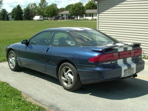 1995 Ford Probe - A blue coupe with white racing stripes is parked on a driveway next to a building.