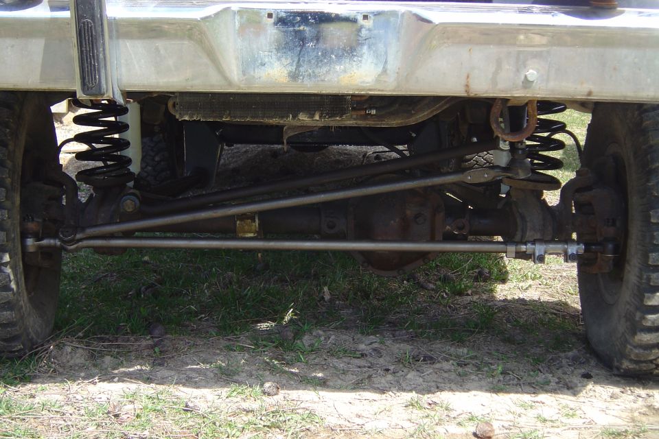 Underside front view of a truck's solid front axle with coil springs, steering linkage, and differential