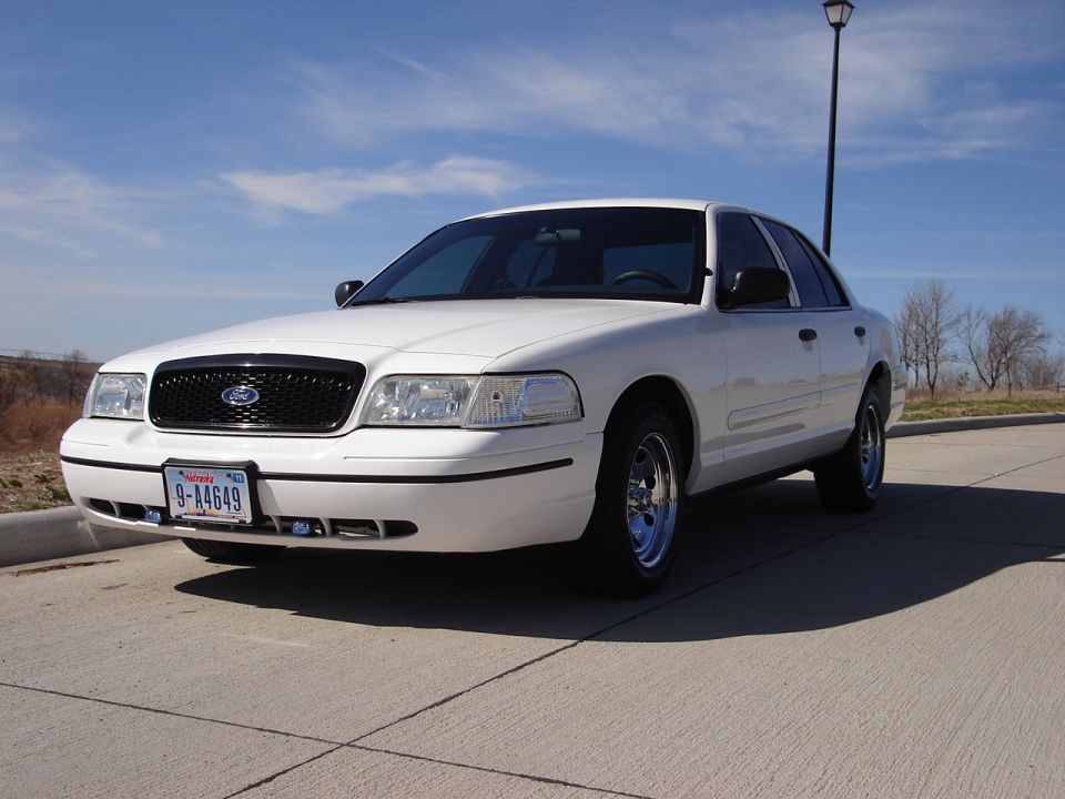 White sedan parked on pavement, blue sky overhead. License plate reads 9-A4649