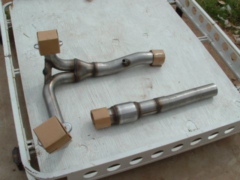 1990 Ford Bronco - Exhaust system part shown on a white surface, with cardboard protectors on the ends.