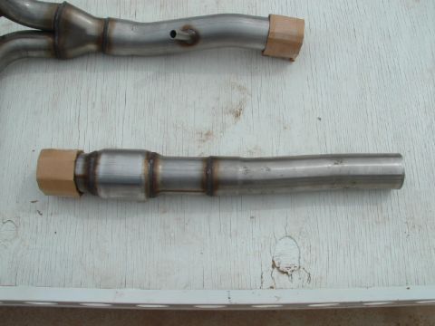 1990 Ford Bronco - Two stainless steel exhaust pipes, one with a catalytic converter, are laid out on a wooden surface.
