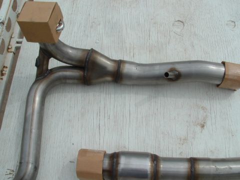 1990 Ford Bronco - Close-up of a stainless steel exhaust system part, likely a Y-pipe, with protective caps.