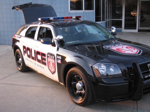 1991 Ford LTD Crown Victoria - Front three-quarter view of a black-and-white Dodge Magnum police wagon with a push bar, light bar, and ram-shield hood decal.