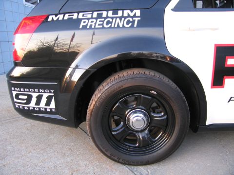 1991 Ford LTD Crown Victoria - Close-up of a black-and-white police wagon's rear quarter with a black wheel, MAGNUM PRECINCT badge, and EMERGENCY 911 RESPONSE decal.