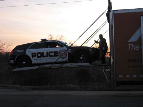 1991 Ford LTD Crown Victoria - black-and-white POLICE Dodge Magnum wagon sits on a tilted trailer ramp at dusk while a man secures it.