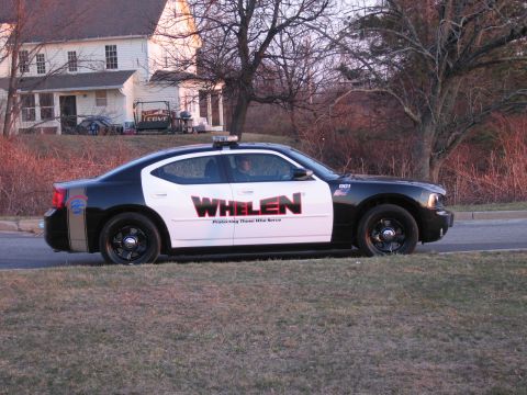 1991 Ford LTD Crown Victoria - Side profile of a black-and-white Dodge Charger police sedan marked WHELEN, parked on grass in front of a house at dusk.
