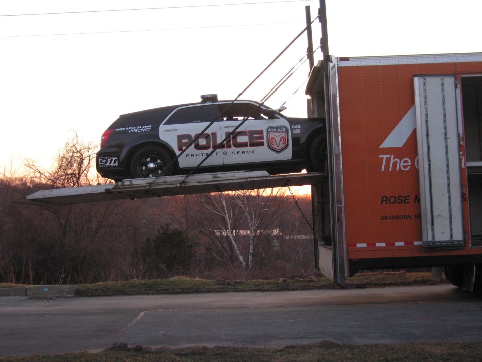 Black and white POLICE-marked SUV loaded on an enclosed orange auto carrier ramp