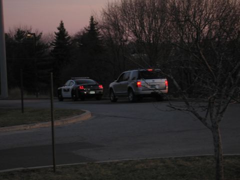 1991 Ford LTD Crown Victoria - police sedan and a silver Ford pickup fitted with a light bar sit on a curved driveway in dim dusk light.