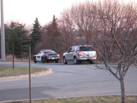 1991 Ford LTD Crown Victoria - black-and-white police Dodge Charger parked beside a silver Ford Explorer Sport Trac with a roof light bar on a tree-lined curve.