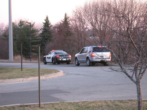 1991 Ford LTD Crown Victoria - police sedan and a silver Ford pickup, both with emergency light bars, parked along a curved road at dusk.