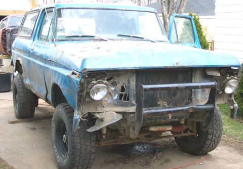 1978 Ford Bronco - This blue SUV is missing its front end components and has its driver's door open.
