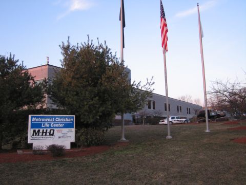 1991 Ford LTD Crown Victoria - low building behind a 'Metrowest Christian Life Center / MHQ Municipal Headquarters' sign with three flagpoles, one flying a US flag.