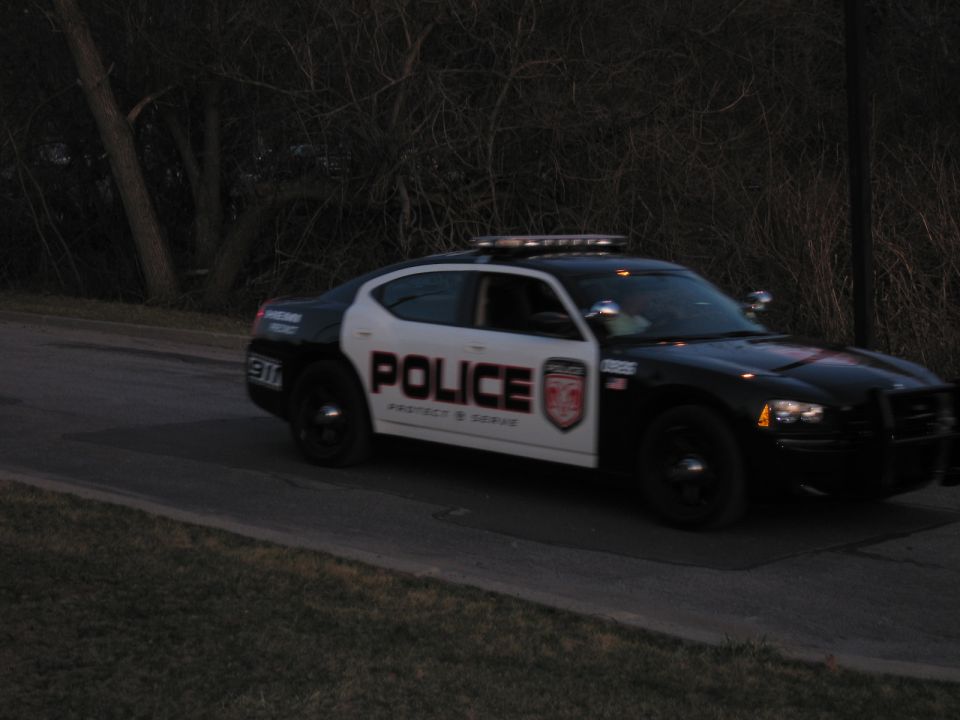 Black and white POLICE-marked Dodge Charger parked on a roadside at dusk