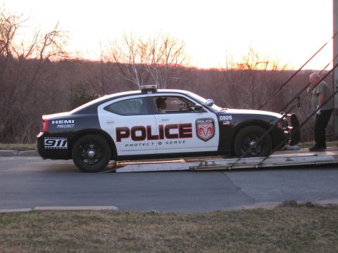 1991 Ford LTD Crown Victoria - black-and-white POLICE Dodge Charger sits on an auto-transport ramp as a man stands beside it at sunset.