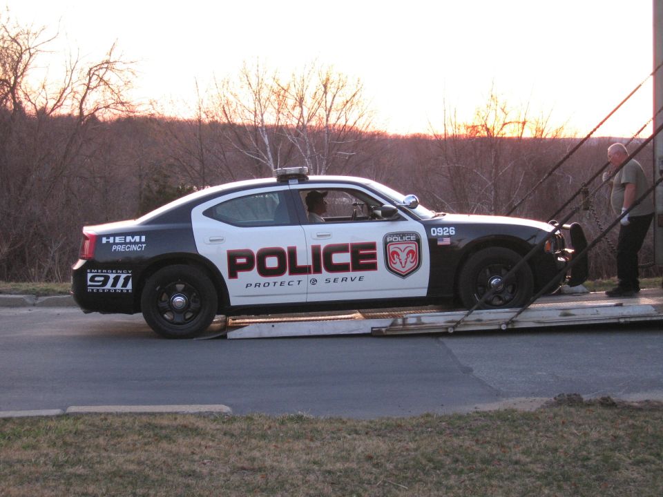 Police Dodge Charger being loaded onto an auto carrier ramp at sunset
