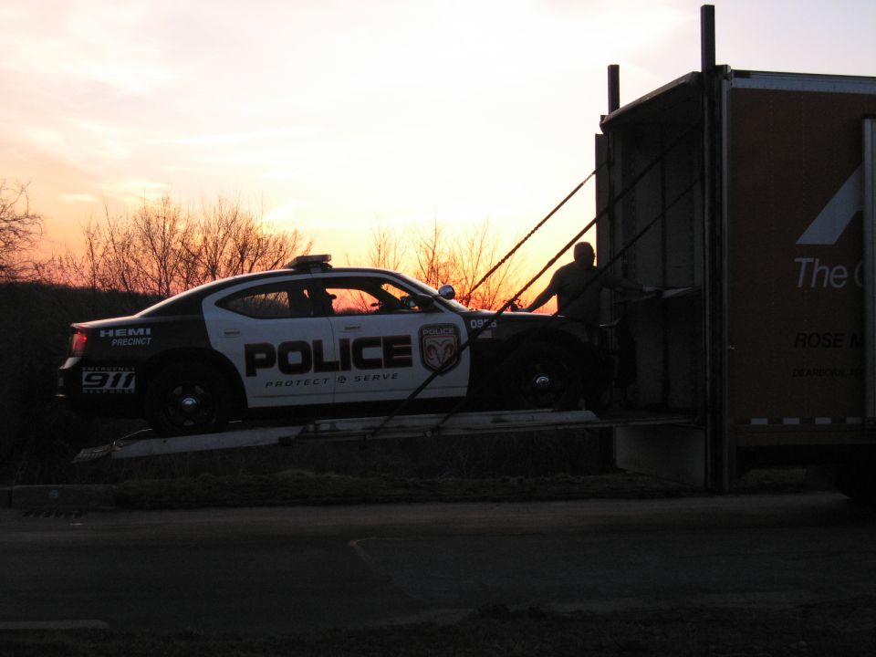 Police Dodge Charger on a carrier ramp silhouetted against a sunset sky