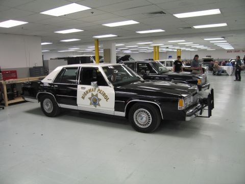 1991 Ford LTD Crown Victoria - black-and-white Ford LTD Crown Victoria marked 'Highway Patrol' with a star emblem and push bar displayed indoors among other cars.