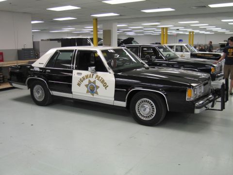 1991 Ford LTD Crown Victoria - black-and-white Ford LTD Crown Victoria 'Highway Patrol' sedan with star emblem and push bar parked on a showroom-style floor.