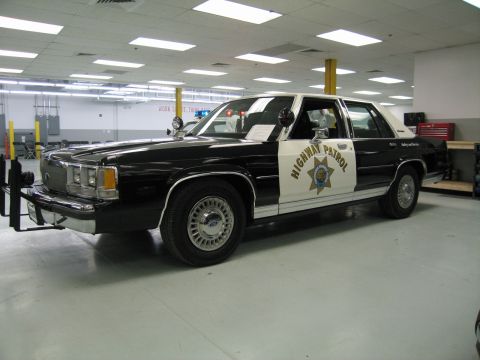 1991 Ford LTD Crown Victoria - black-and-white Ford LTD Crown Victoria 'Highway Patrol' sedan with star emblem and front push bar displayed on a showroom floor.