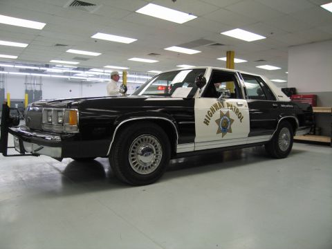 1991 Ford LTD Crown Victoria - black-and-white Ford LTD Crown Victoria 'Highway Patrol' sedan with push bar displayed indoors as a man stands beside it.