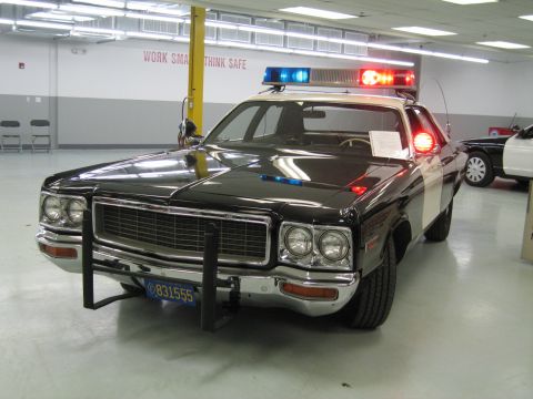 1991 Ford LTD Crown Victoria - restored black-and-white Dodge police cruiser with roof light bar and push bumper sits on a shop floor under fluorescent lights.