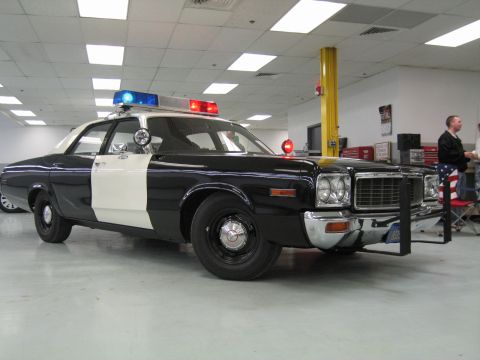 1991 Ford LTD Crown Victoria - black-and-white classic police sedan with roof light bar and spotlight sits in a brightly lit garage, a man standing in the background.