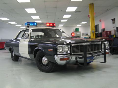1991 Ford LTD Crown Victoria - Front three-quarter view of a restored black-and-white police cruiser with chrome push bumper and lit light bar on a shop floor.