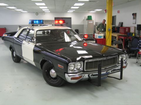 1991 Ford LTD Crown Victoria - restored black-and-white Dodge police cruiser with push bumper and light bar on a shop floor while a man works behind it.
