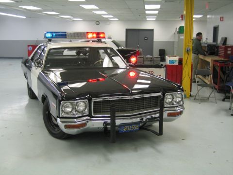 1991 Ford LTD Crown Victoria - black-and-white police cruiser with its red and blue light bar lit, push bumper and chrome trim, parked in a workshop.