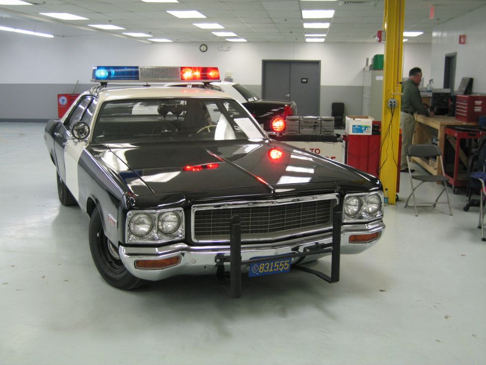 Front three-quarter of black police car with lit light bar in a garage