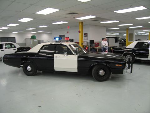 1991 Ford LTD Crown Victoria - Full side profile of a black-and-white classic police sedan with white door panel and roof light bar on a shop floor.