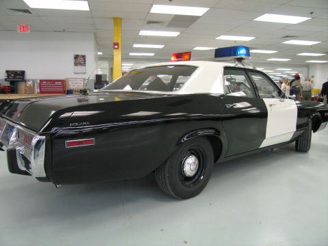 1991 Ford LTD Crown Victoria - Rear three-quarter view of a black-and-white Dodge Polara police cruiser, POLARA script on the fender, with lit roof light bar.