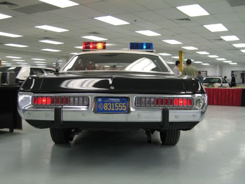 1991 Ford LTD Crown Victoria - Direct rear view of a black-and-white police cruiser with lit emergency lights and California plate, people gathered behind it.