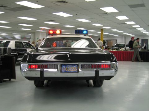 1991 Ford LTD Crown Victoria - Direct rear view of a black-and-white police cruiser with full-width taillights and California plate in a busy display room.