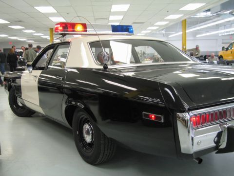 1991 Ford LTD Crown Victoria - Rear three-quarter view of a black-and-white Dodge Polara police cruiser with white roof, POLARA script and lit roof light bar.