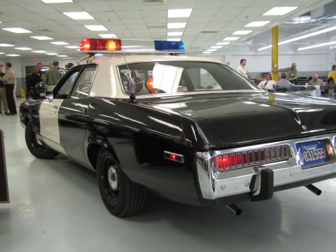 1991 Ford LTD Crown Victoria - Rear three-quarter view of a black-and-white police cruiser with white roof and door panel, parked among onlookers in a display hall.