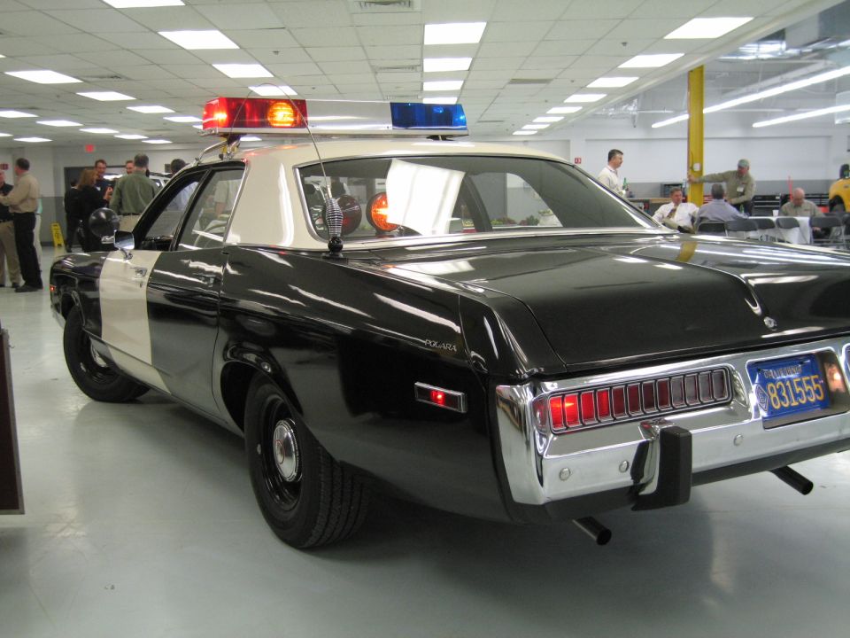 Rear three-quarter of black-and-white police car among people in a hall