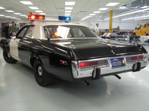 1991 Ford LTD Crown Victoria - Rear three-quarter view of a black-and-white police cruiser with full-width taillights and amber roof light in a crowded hall.