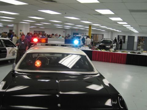 1991 Ford LTD Crown Victoria - Close view over a police cruiser's roof light bar and rear window, looking across a crowded display hall with another cruiser.