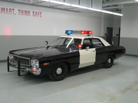1991 Ford LTD Crown Victoria - black-and-white police sedan with a roof light bar sits in a garage beneath a wall reading SMART, THINK SAFE.
