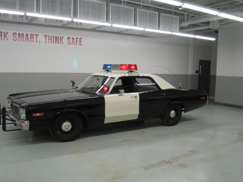 1991 Ford LTD Crown Victoria - black-and-white police sedan with illuminated roof beacons sits in a garage under a wall reading WORK SMART, THINK SAFE.