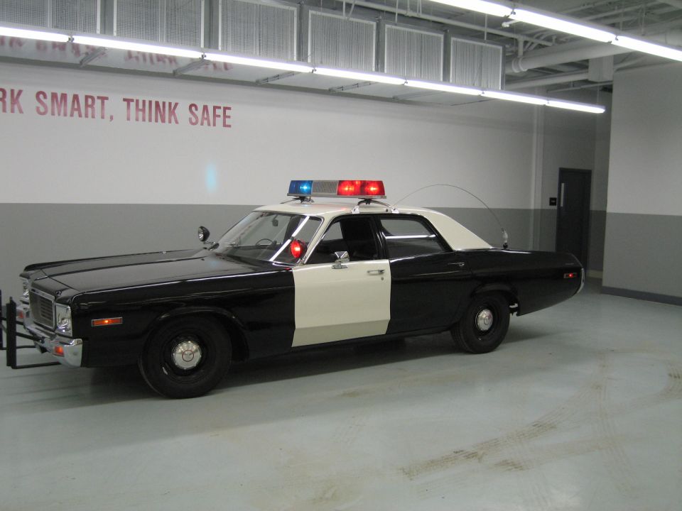 Front-three-quarter view of a black-and-white police sedan with lit roof beacons in a garage