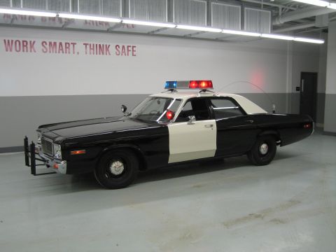 1991 Ford LTD Crown Victoria - black-and-white police sedan displays red and blue roof lights in a garage with WORK SMART, THINK SAFE on the wall.