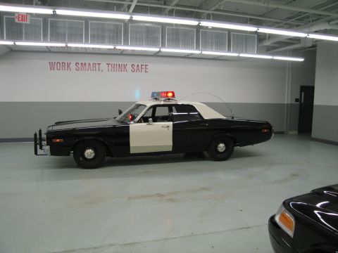1991 Ford LTD Crown Victoria - black-and-white police sedan shown in side profile with a lit roof light bar inside a garage.