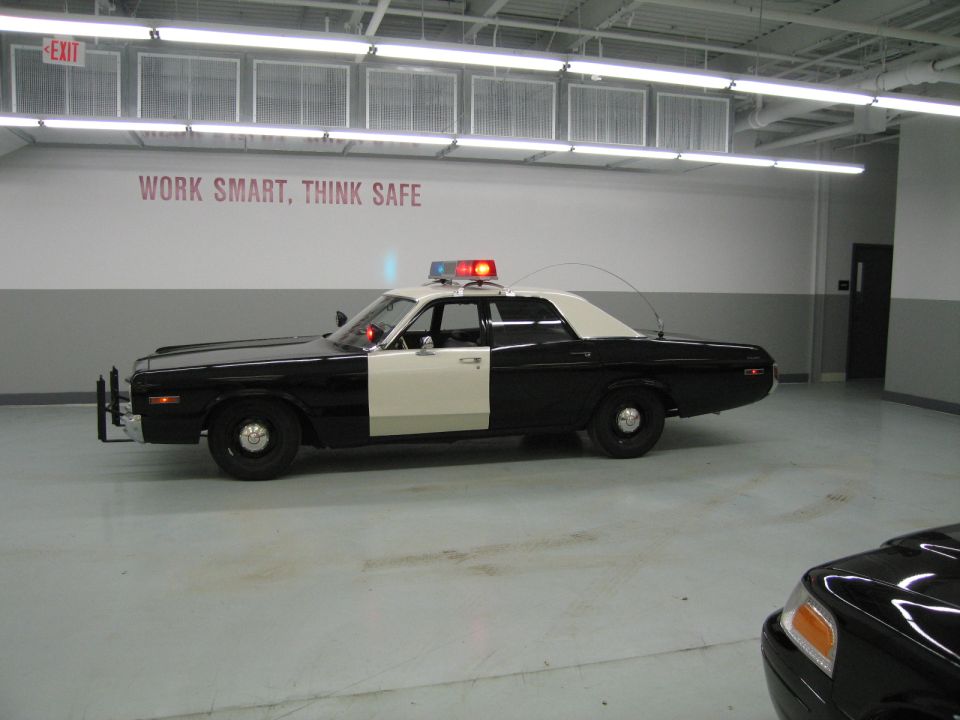 Side profile of a black-and-white police sedan with roof light bar in a garage